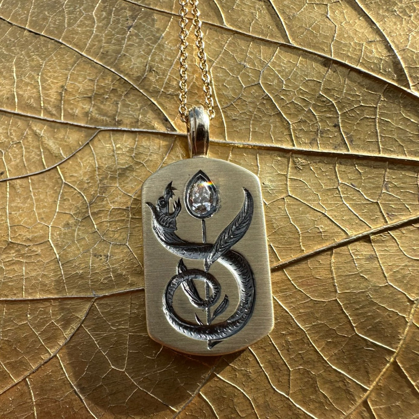 Castro Smith back of silver dog tag pendant engraved with a snake wrapped around a diamond flower. Hung on a silver chain.