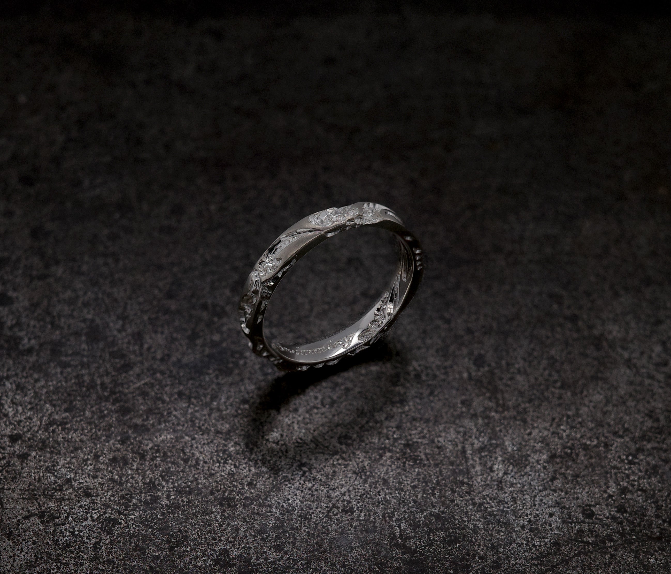 Wave Band (4mm) ring displayed on a textured dark surface, showcasing its intricate design.