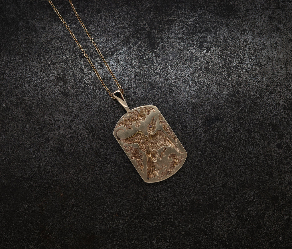 Gold bird pendant with intricate engravings hanging from a delicate gold chain on dark background