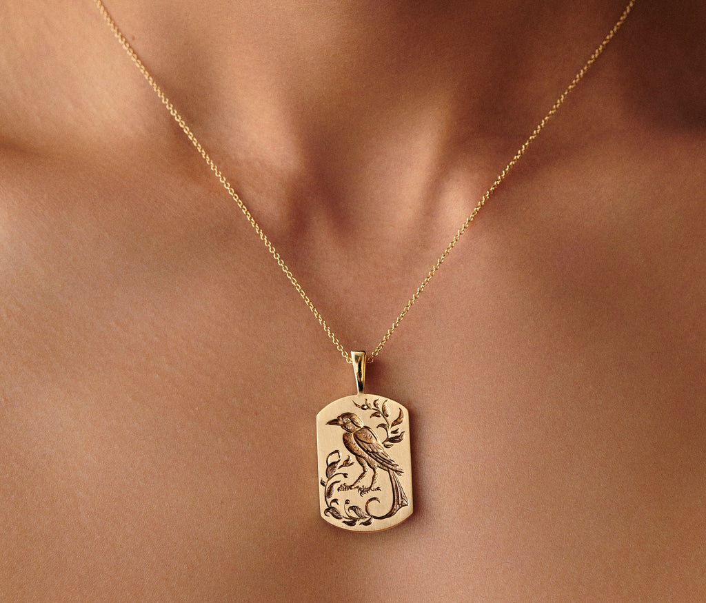 Gold bird pendant necklace with intricate engraved design on a delicate chain worn on the neck