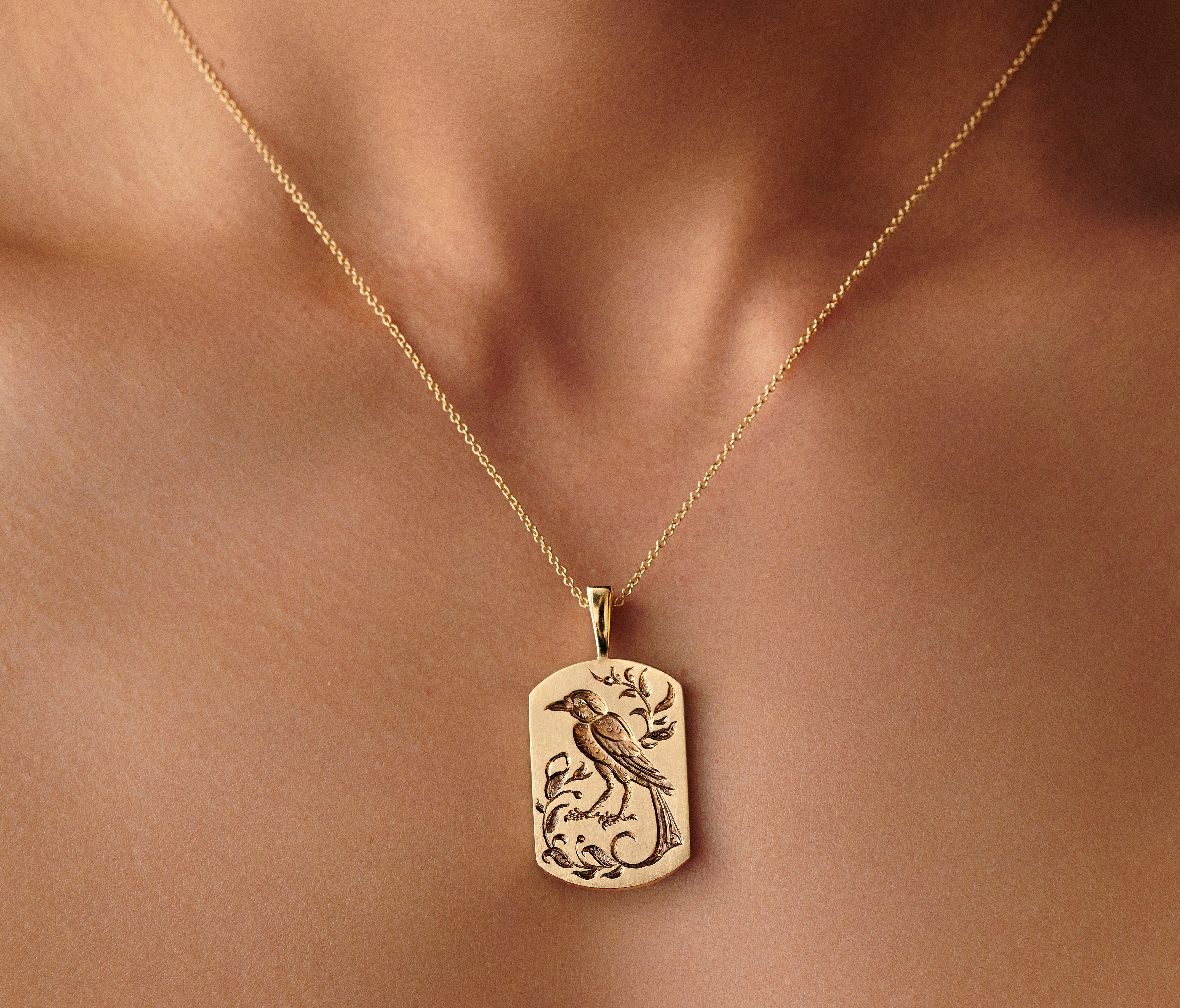 Gold bird pendant necklace with intricate engraved design on a delicate chain worn on the neck