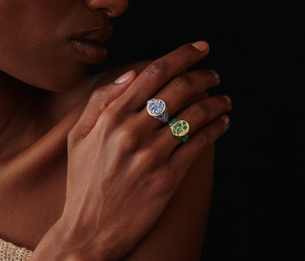 Close-up of a hand wearing two Heart Signet Mini rings with intricate healing symbol designs on a dark background
