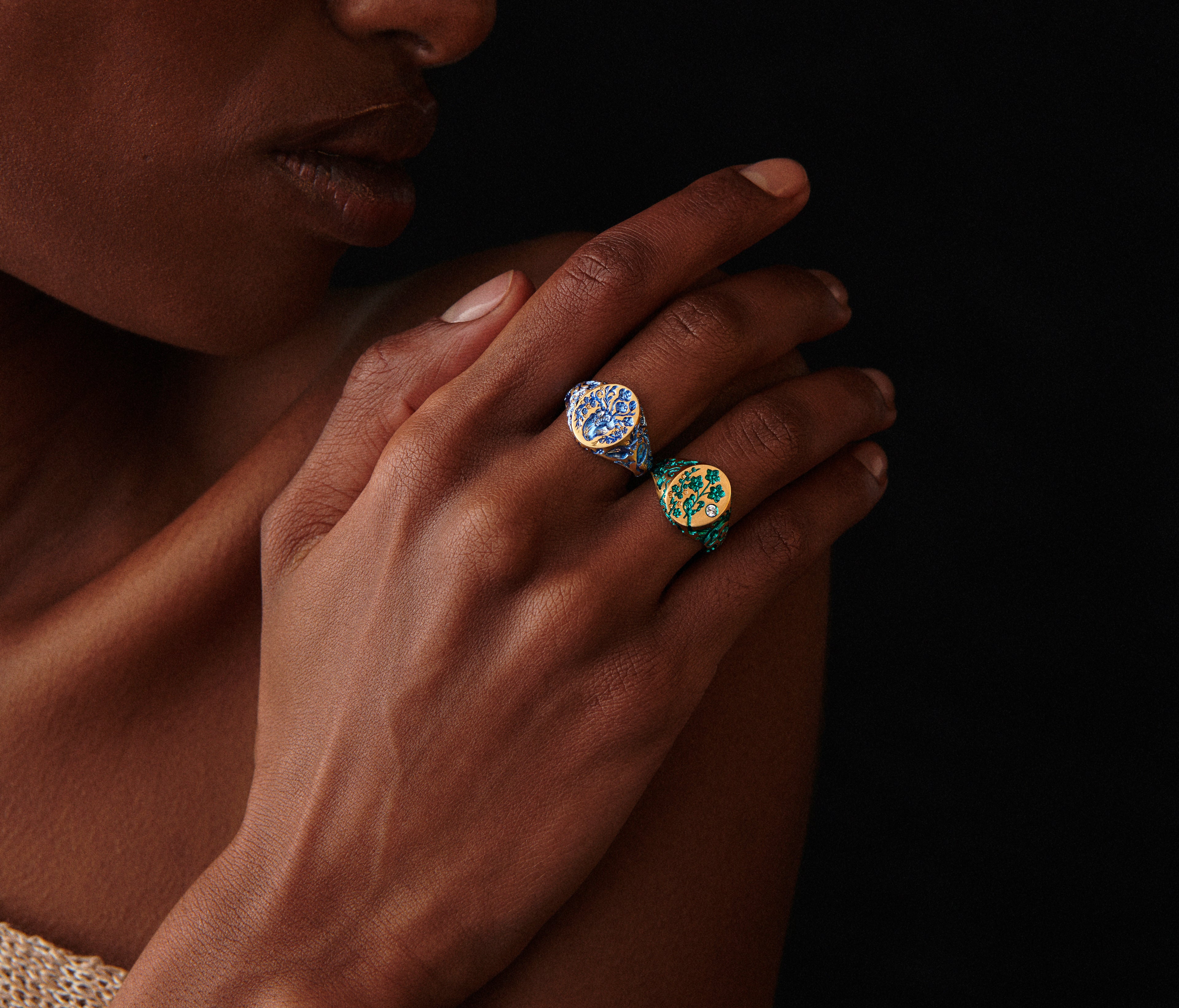 Close-up of a hand wearing two Heart Signet Mini rings with intricate healing symbol designs on a dark background