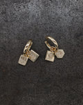 Gold-toned tiny hoop earrings with engraved pumpkin, flower, and bug charms on dark textured background