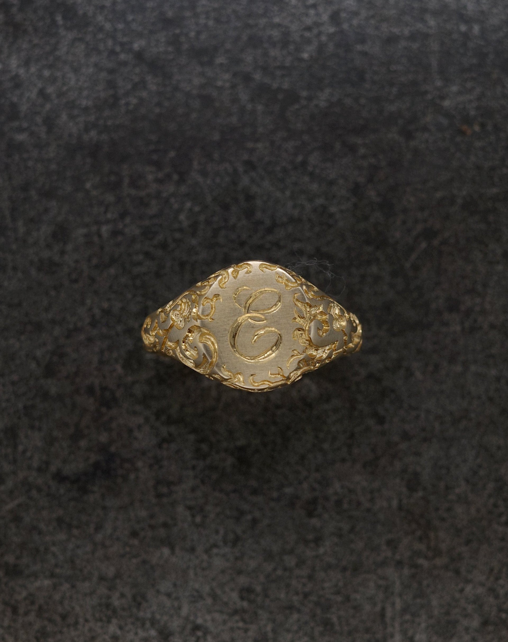 E Minor Signet Ring in gold with intricate design and custom initials on a textured background.