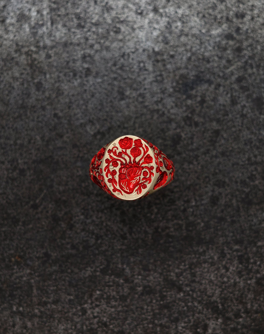Mini heart signet ring with red floral and anatomical heart design on textured dark background
