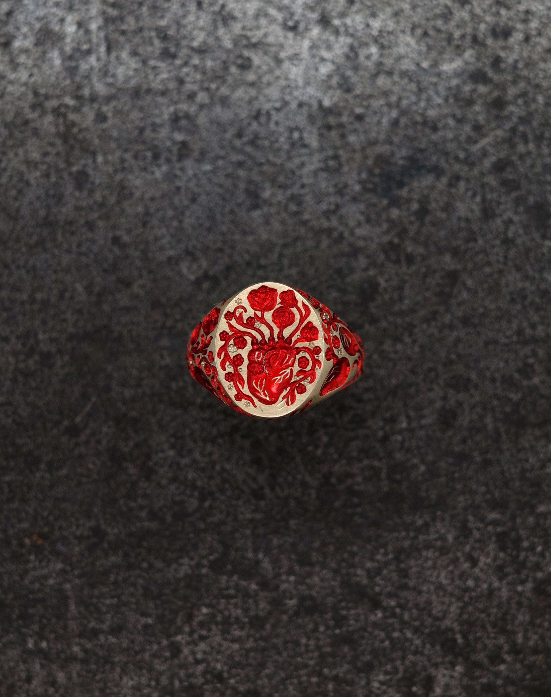 Mini heart signet ring with red floral and anatomical heart design on textured dark background