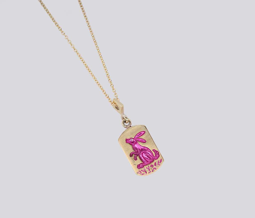 Gold pendant necklace featuring a hand-engraved pink rabbit and carrot design with ceramic plating and gemstone detail