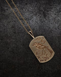 Gold bird pendant necklace with intricate floral engraving on a dark textured background