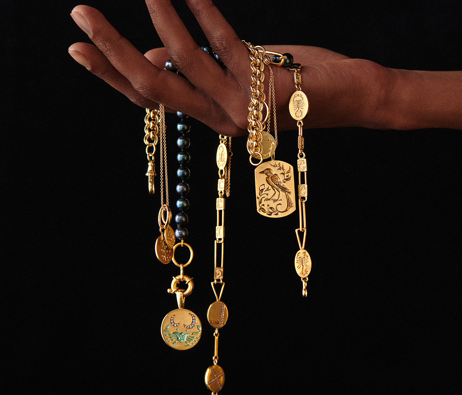 Hand holding multiple gold necklaces with intricate pendants, featuring a detailed bird pendant against a black background