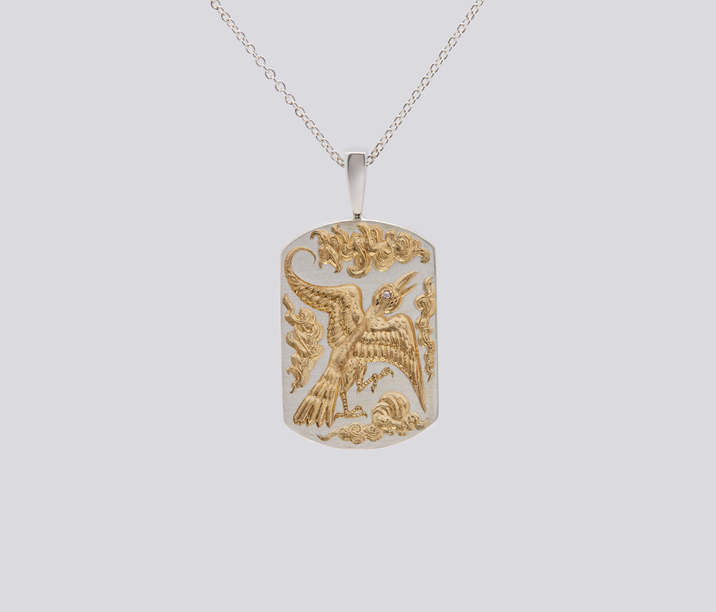 Silver and gold bird pendant necklace with intricate engraved design on a rectangular tag background