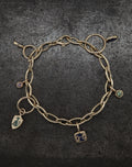 Gold chain bracelet with winged key charms and colored gemstone accents on dark textured background