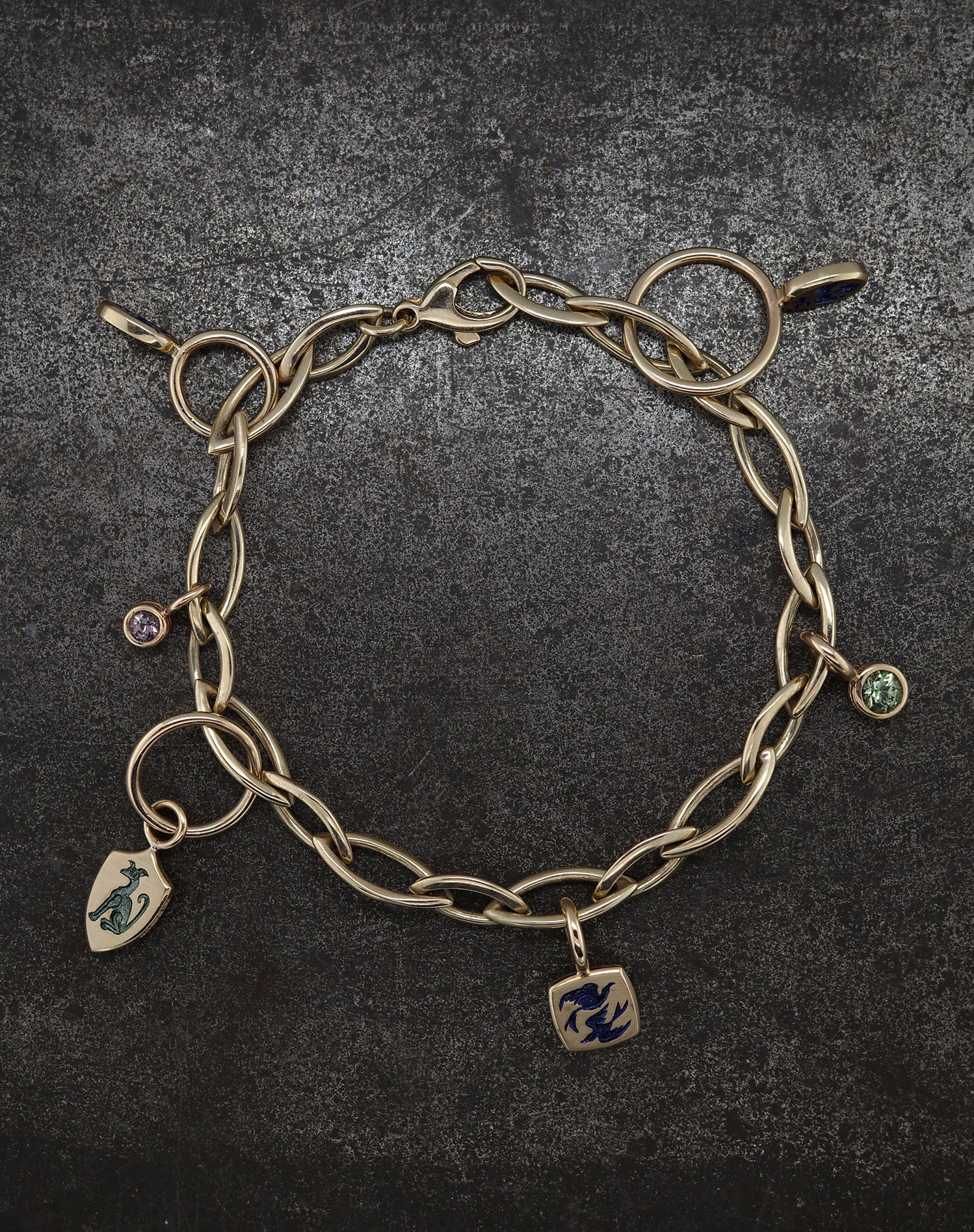 Gold chain bracelet with winged key charms and colored gemstone accents on dark textured background
