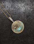 Gold pendant necklace with diamond-adorned crescent moons and a turquoise crab design on a textured background