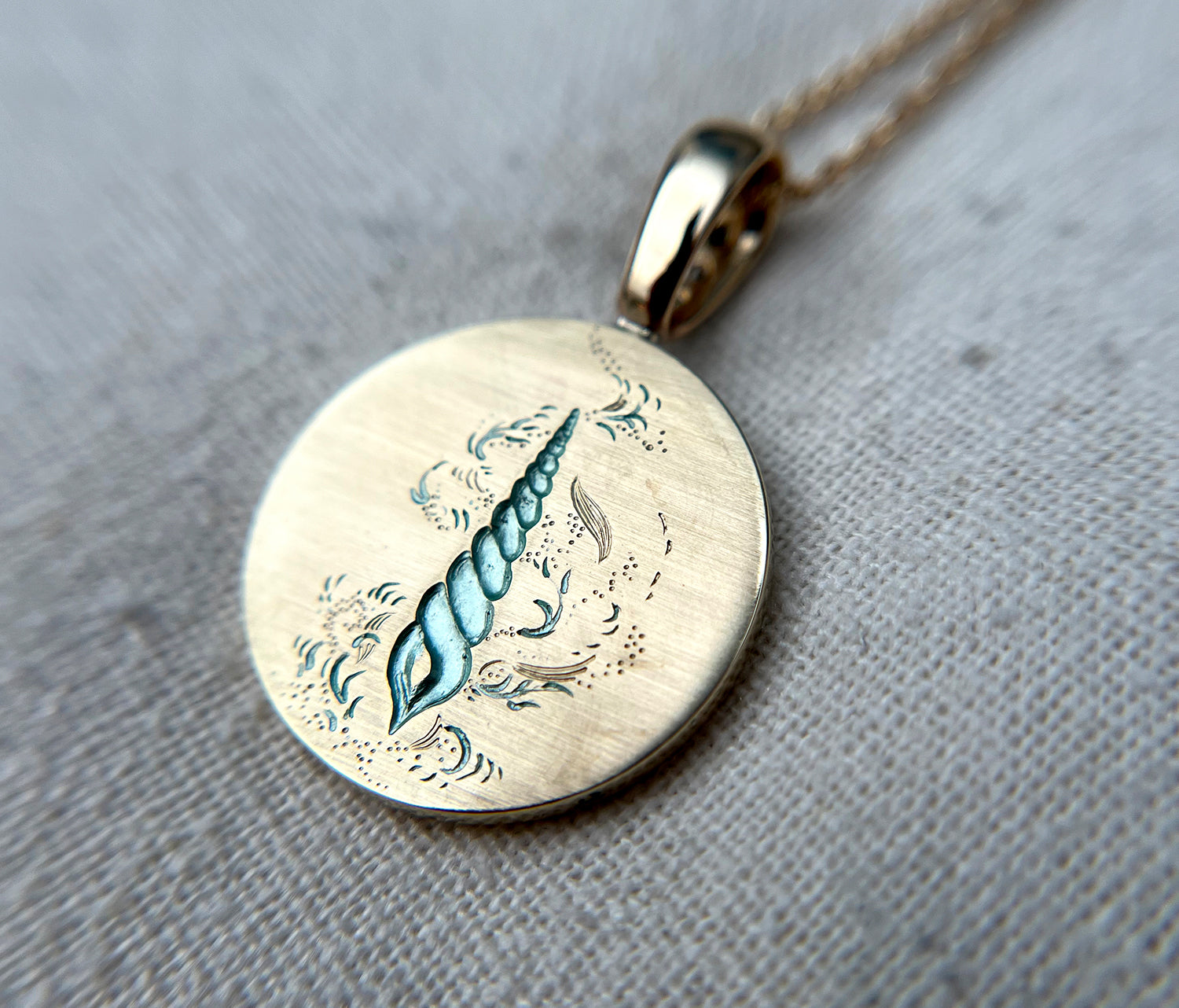 Close-up of gold pendant featuring an engraved seashell design with a diamond bale on a delicate chain
