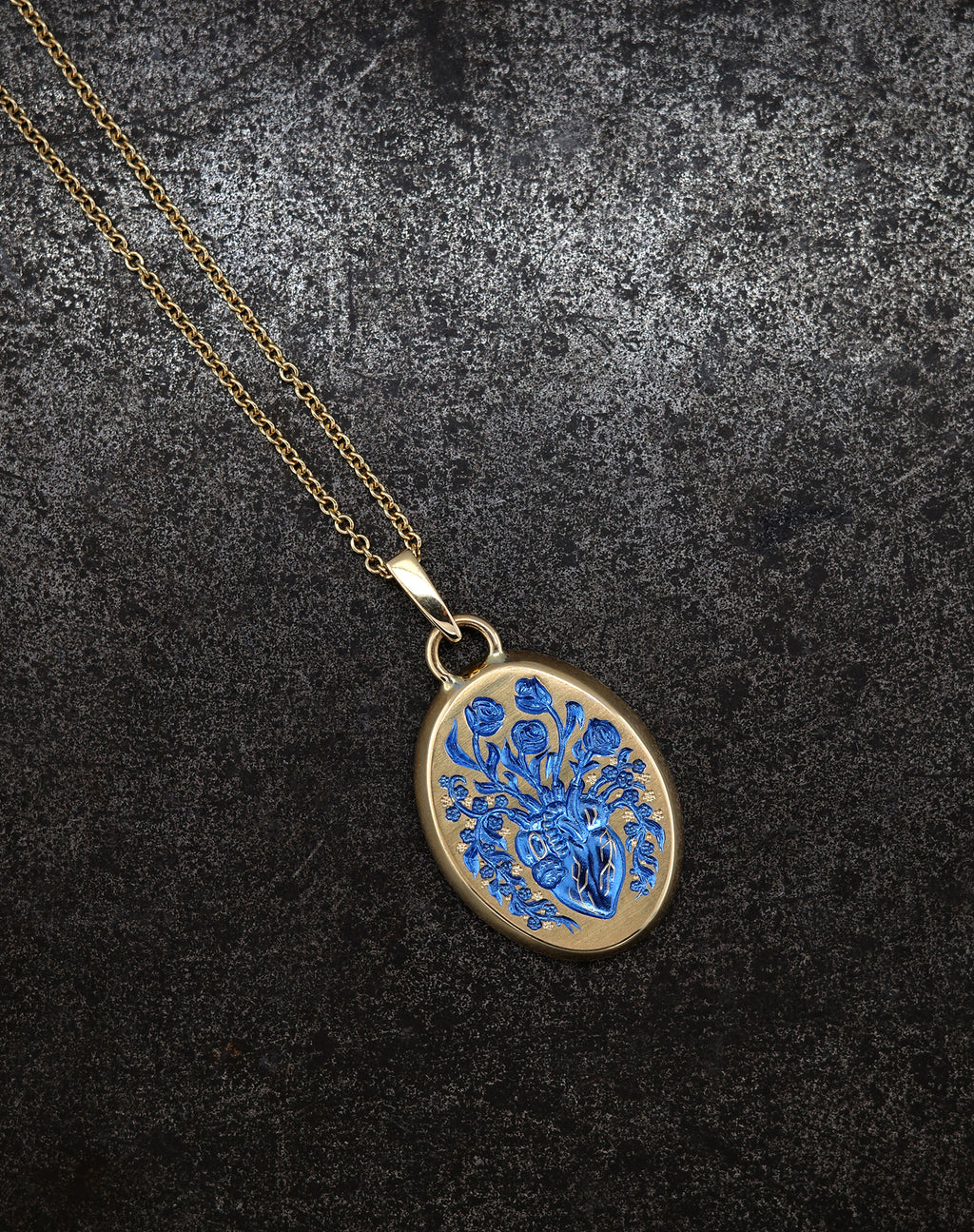 Gold heart pendant necklace with intricate blue floral design on textured dark background