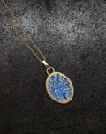 Gold heart pendant necklace with intricate blue floral design on textured dark background