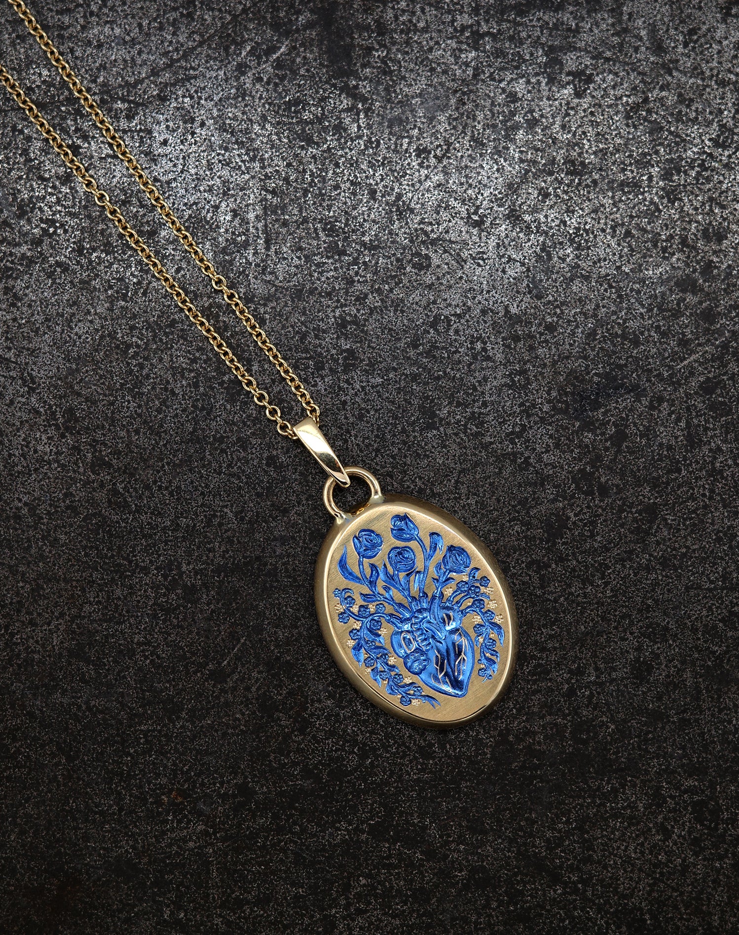 Gold heart pendant necklace with intricate blue floral design on textured dark background