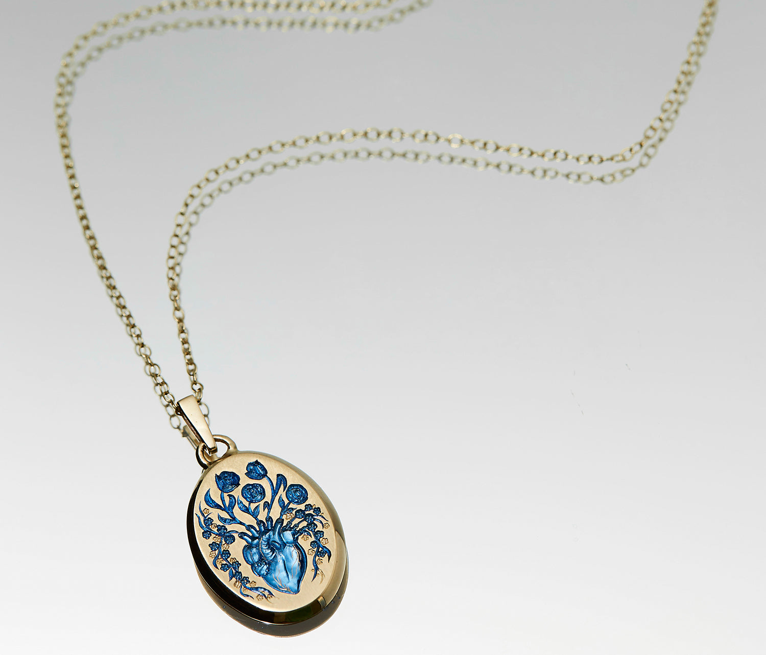 Small gold heart pendant necklace with blue anatomical heart and floral design on oval locket