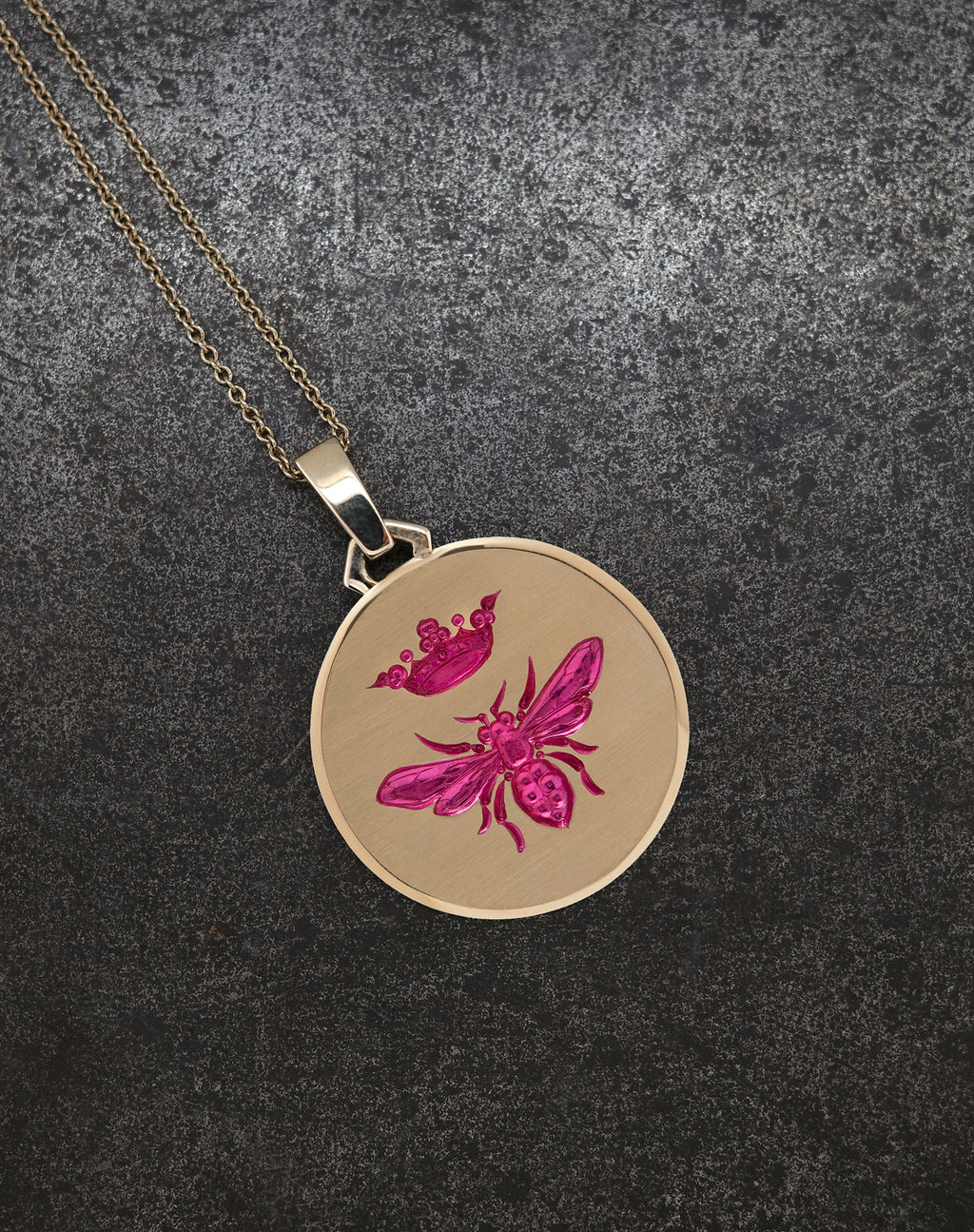 Gold Queen Bee Pendant with pink bee and crown engraving on textured black background