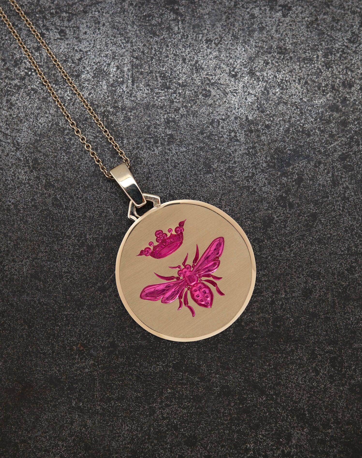 Gold Queen Bee Pendant with pink bee and crown engraving on textured black background