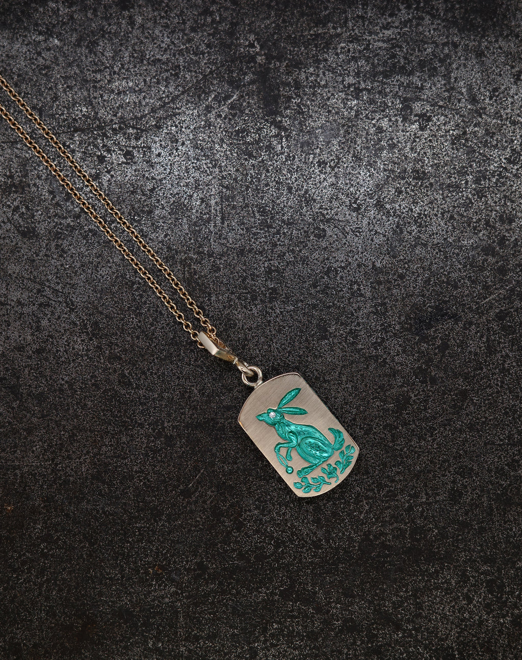 Pendant necklace with hand-engraved turquoise rabbit and foliage on a silver ceramic-plated background with gold chain