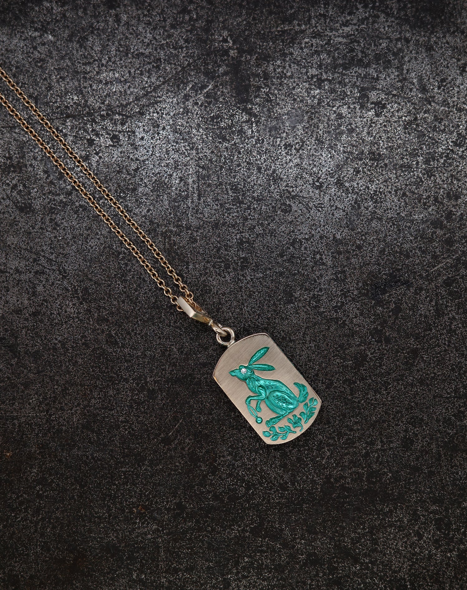 Pendant necklace with hand-engraved turquoise rabbit and foliage on a silver ceramic-plated background with gold chain