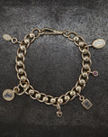 Gold chain bracelet with assorted charms including ancient talisman, hand, star, and purple gem on dark background