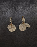 Gold hoop earrings with engraved palm tree and small charm featuring bugs and fruits design on dark background
